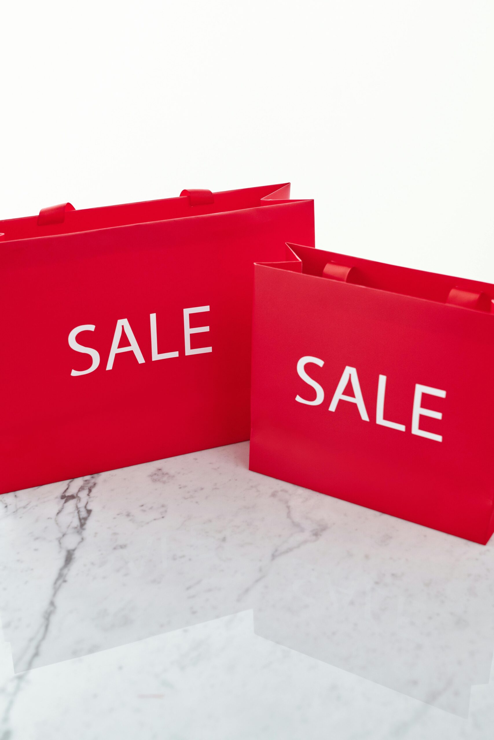 Vibrant red shopping bags with 'SALE' text placed on a marble surface, perfect for promotions.